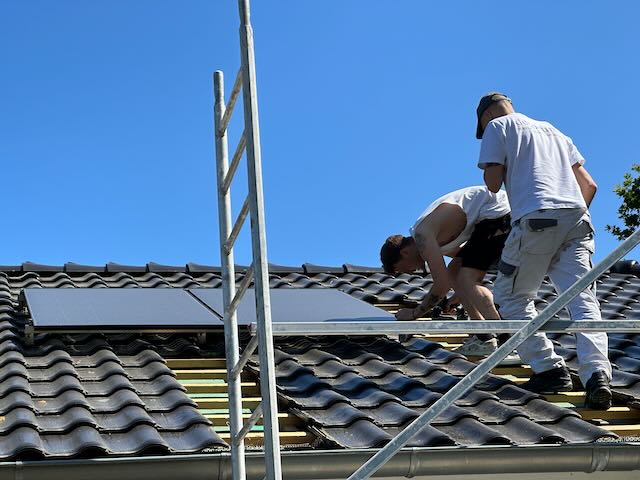Zwei Menschen montieren eine Solarzelle auf dem Dach.