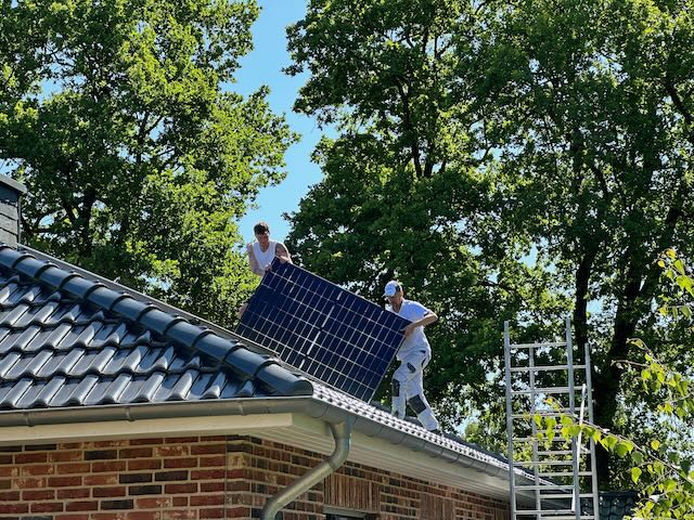 Zwei Menschen heben eine Solarzelle auf ein Dach.
